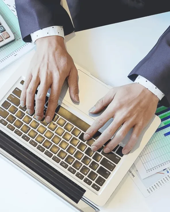 A person in a suit typing on a laptop keyboard.