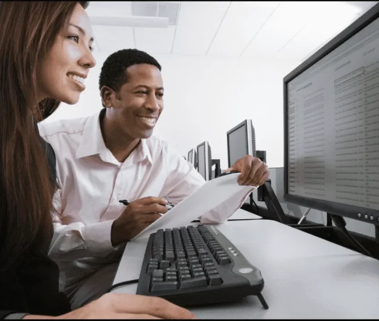 Two people collaborating at a computer, smiling and discussing documents.