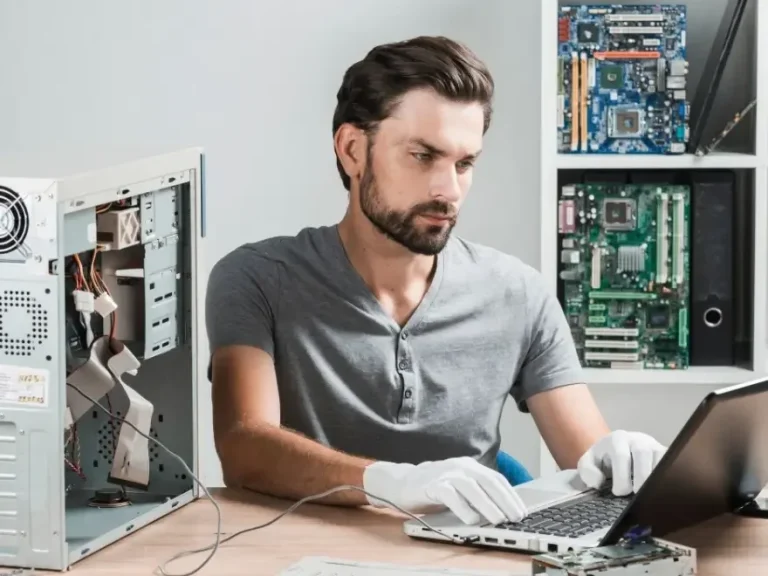 Second Chance Employment A technician repairs a computer while working on a laptop, wearing gloves.