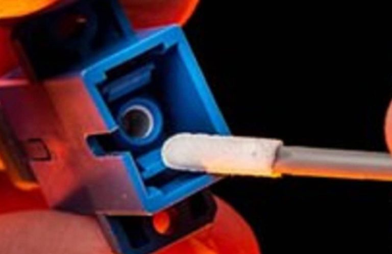 fiber optic repair: Close-up of a hand inserting a cotton swab into a blue electronic connector.