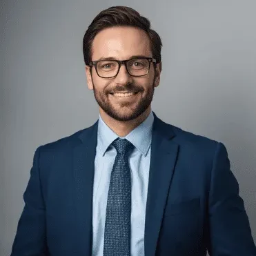Michael T Smiling man in a suit and glasses with a blue tie against a gray background.