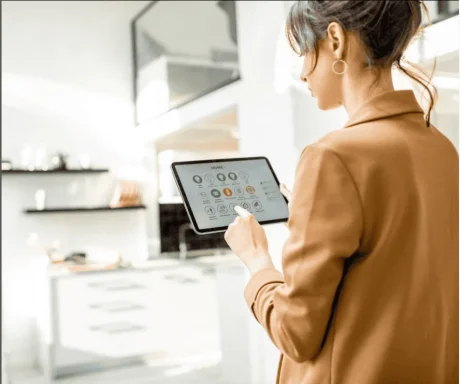 A person in a brown jacket holds a tablet in a modern kitchen.