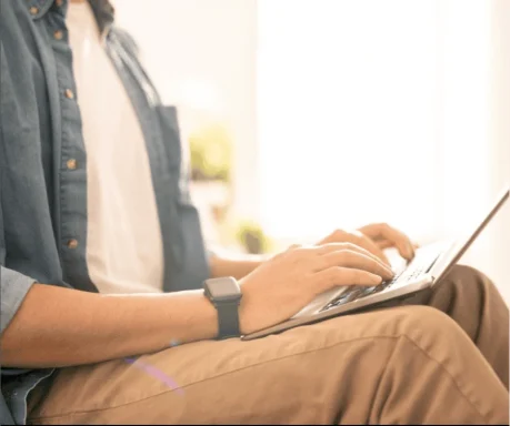 Person typing on a laptop while sitting in a bright environment.