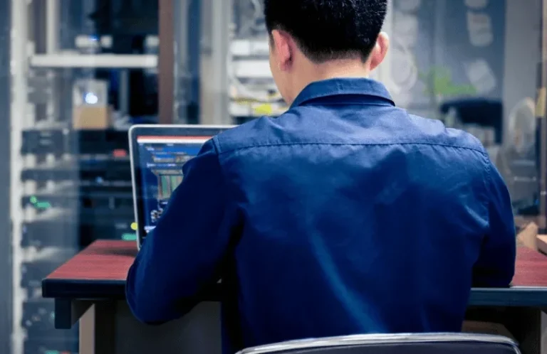 Person working on a laptop in a tech environment, viewed from behind.