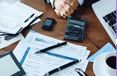 Close-up of a desk with papers, a calculator, a tablet, and a coffee cup.